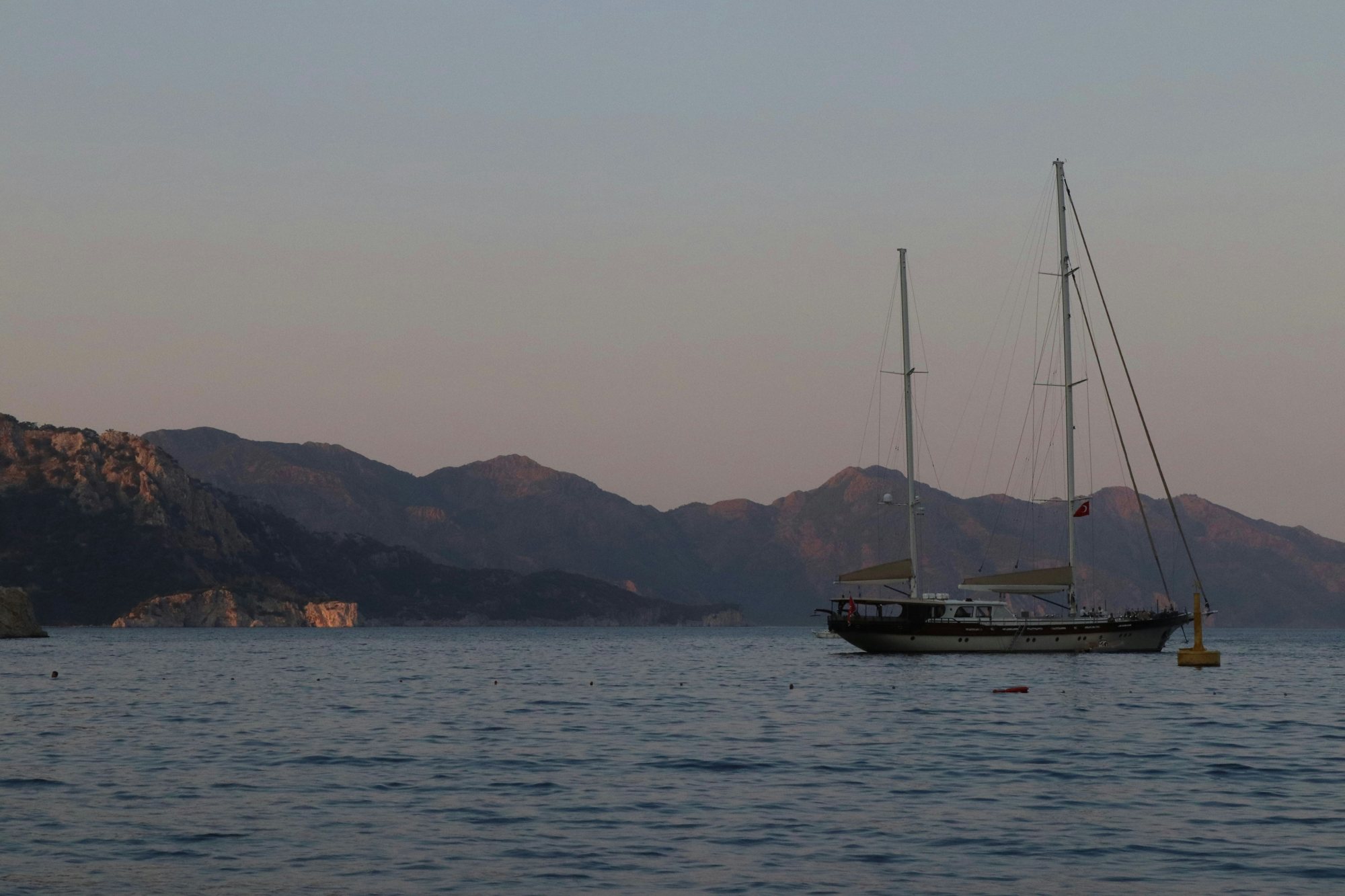A sailboat crossing Pacific coastal water beneath the mountains